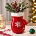 LUMIDED® Christmas mitten ceramic vase full product view on white festive table runner with green Christmas ornament, filled with red berry stems, pine sprigs and white wax flowers, lantern and Christmas tree background